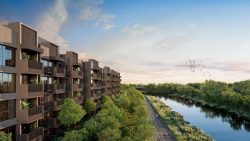 Apartment blocks next to a river with a cycling path and lush greenery under a partly cloudy sky