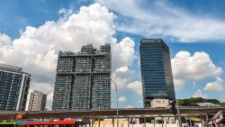 Tall residential apartment blocks and an office tower with MRT track and buses below under a blue sky
