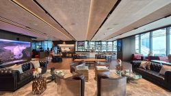 Lounge area with leather sofas, armchairs, glass tables, a large screen, and a bar counter in the background