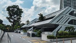 Sloping driveway with white geometric canopy structures and greenery beside residential blocks