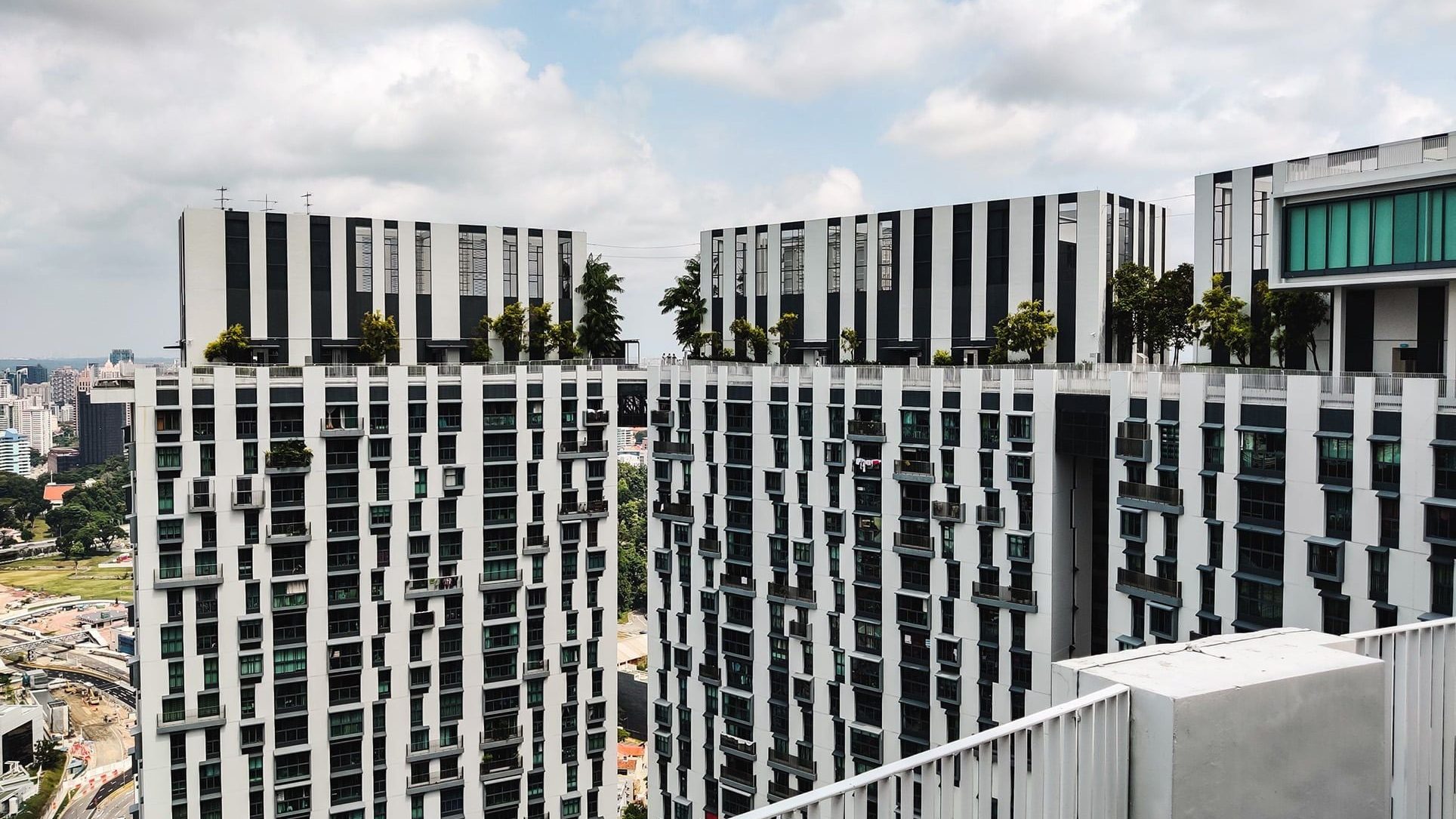 Two high-rise apartment blocks connected by a sky bridge with trees and plants on top
