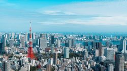 City skyline with a red and white communication tower surrounded by high-rise buildings and water in the background