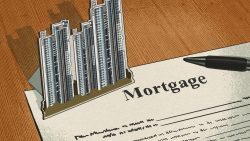 Pen resting on a mortgage document with cutout images of high-rise apartment blocks on a wooden surface