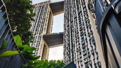 Two residential blocks connected by sky bridges with plants and railings in foreground
