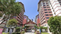Bin Ming Court residential blocks with a central entrance gateway and trees under a clear blue sky