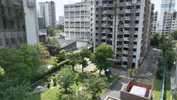 Housing blocks with curved balconies beside a landscaped garden and driveway with parked cars