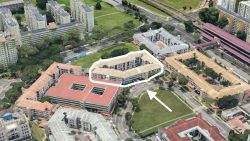 Cluster of low-rise housing blocks outlined beside a curved road and large green field with high-rise blocks nearby