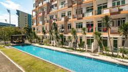 Apartment blocks with balconies facing a swimming pool and landscaped garden area under blue sky